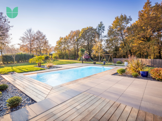 A modern summery garden with a swimming pool and decking around it, and a huge green area with grass.